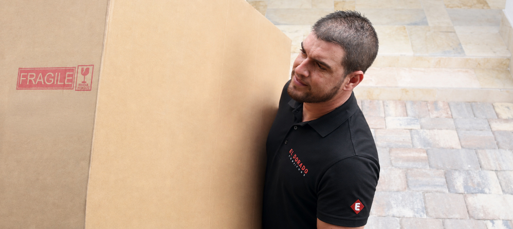 El Dorado Furniture associate carrying a boxed item marked fragile into a home