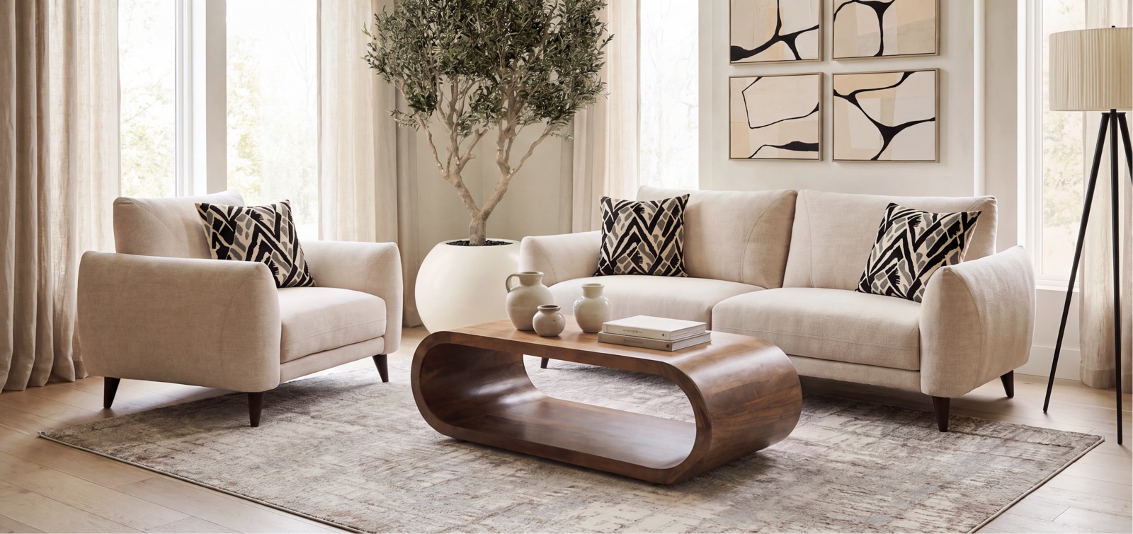 An Italian-inspired living room: a cream sofa and armchair around a curved walnut coffee table, with framed art and a tall olive tree.
